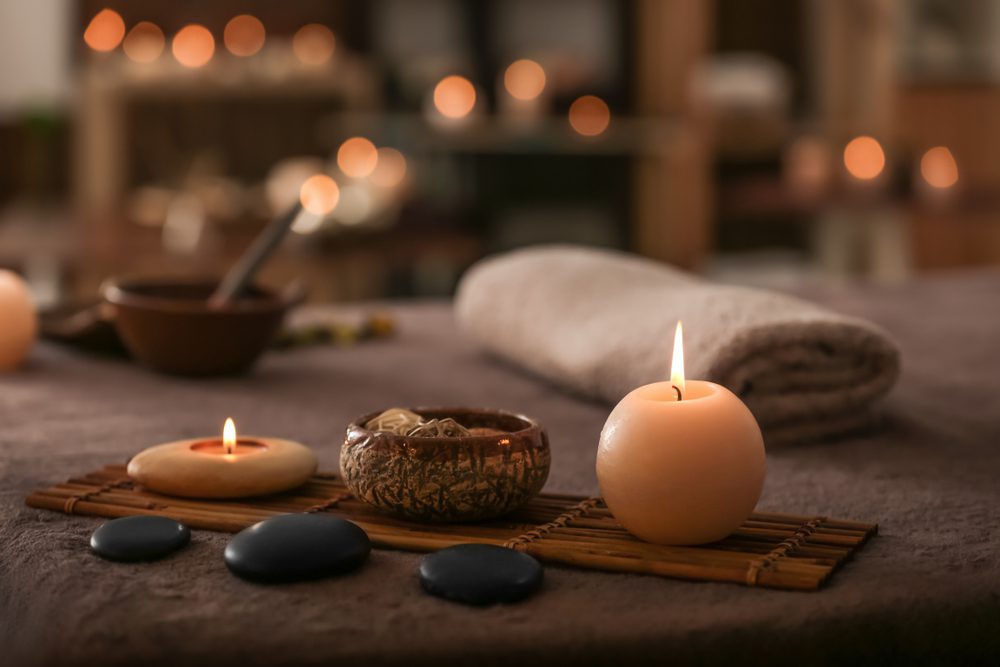 Burning candles, stones and towel on massage table in spa salon